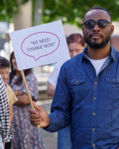 A man is holding up a sign which says We need change now!