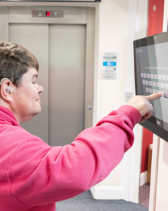A man is using a touch screen mounted on a wall to find some information