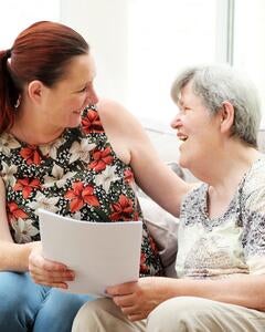 A support worker with an older woman sitting on a sofa smiling at each other
