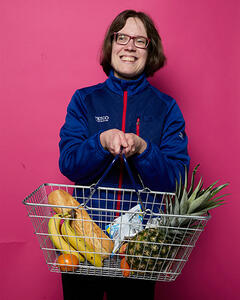 Janis in her Tesco uniform holding a shopping basket of fruit