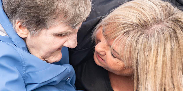 A support worker bending down close to talk to an elderly woman