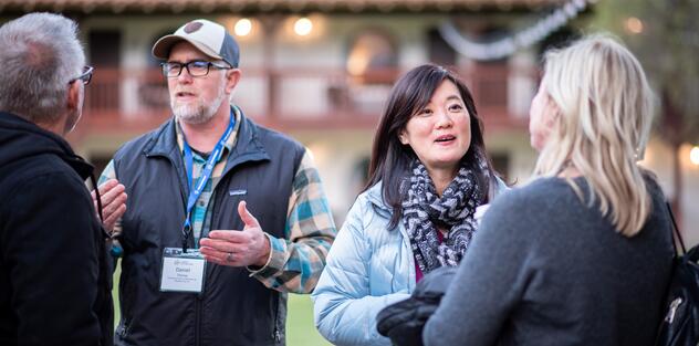 Two pairs of people standing close to one another outside, wearing lanyards, engaging in discussion with one another.
