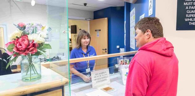 A man is standing at a hospital reception desk talking to a nurse