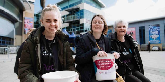 Three fundraisers are sitting on a bench holding Mencap collection buckets