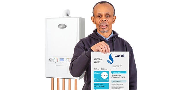 A man holding up a gas bill with a gas boiler behind him