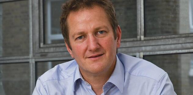 A man in a blue shirt with short dark hair looking at the camera